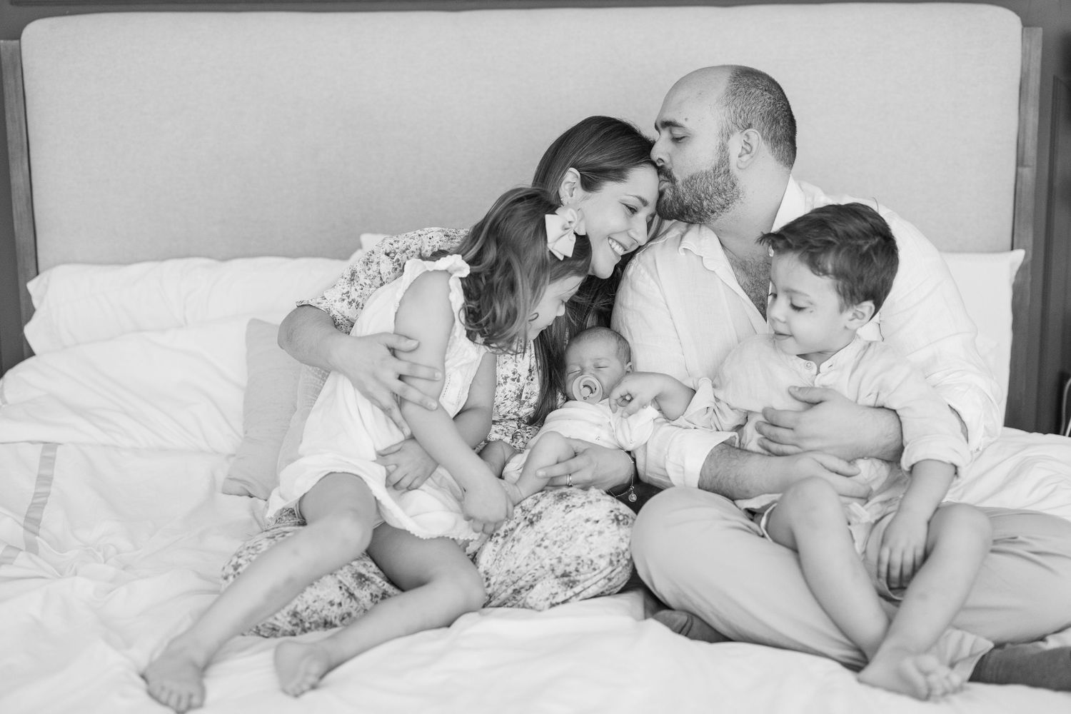 Series of intimate black and white photos showing tender family moments on white bedding.