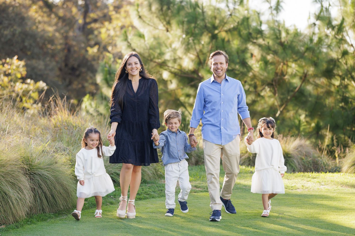 Family walking together on a grassy field during golden hour outdoor photo session.