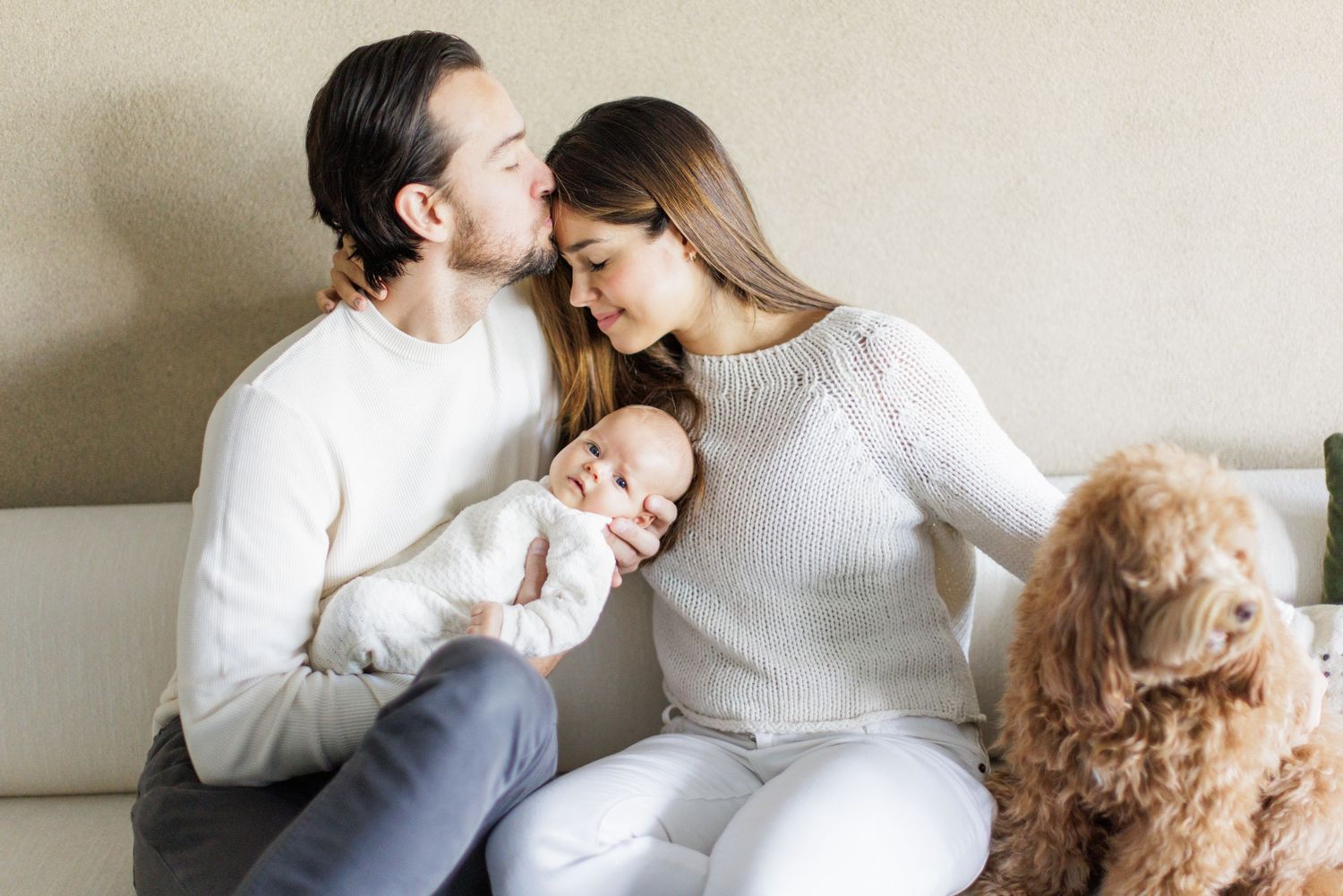 Family sharing tender moments together on white couch in bright room.