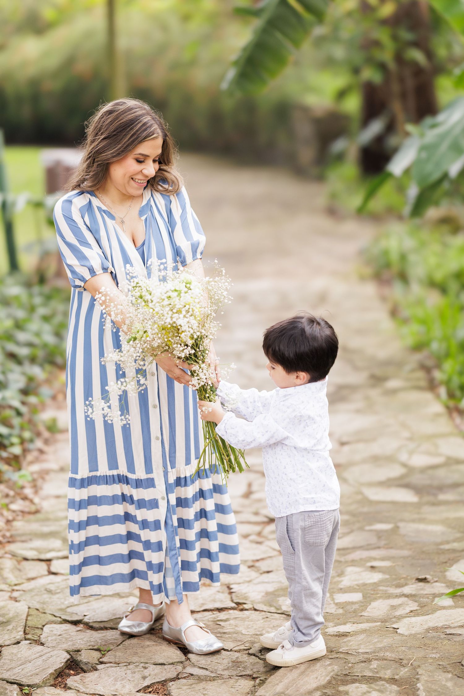 Woman in striped dress holding flowers while child reaches up to touch them.