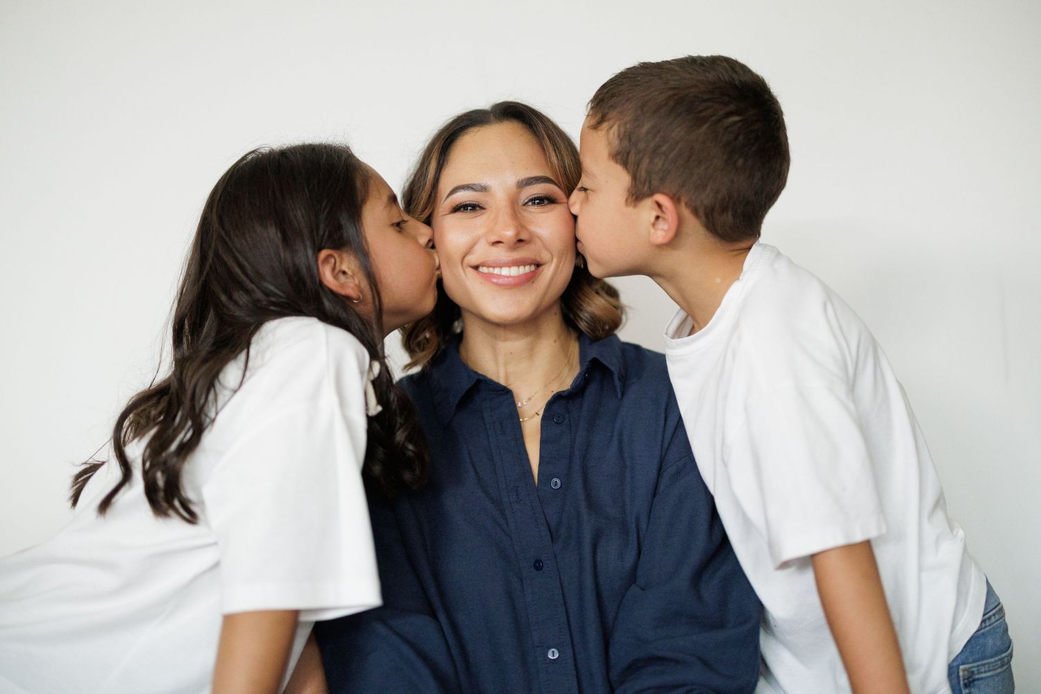 Family members sharing loving embraces in casual attire against white backdrop.