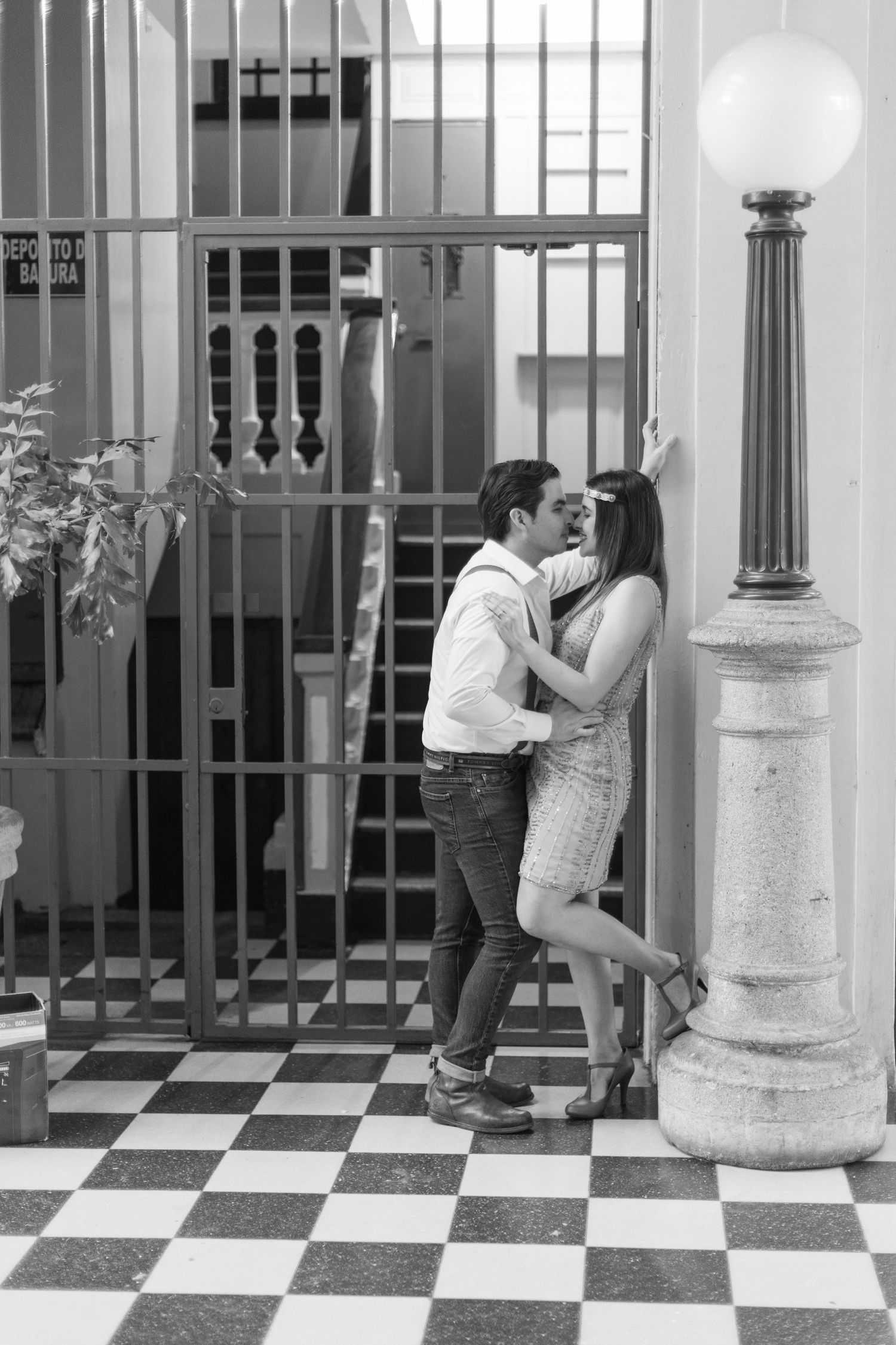 Black and white sequence showing couple posing playfully on checkered floor near iron gates.