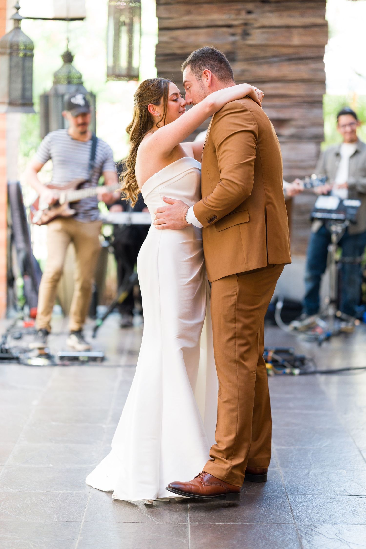Newlyweds dancing together on a dark floor with rustic wooden wall backdrop.