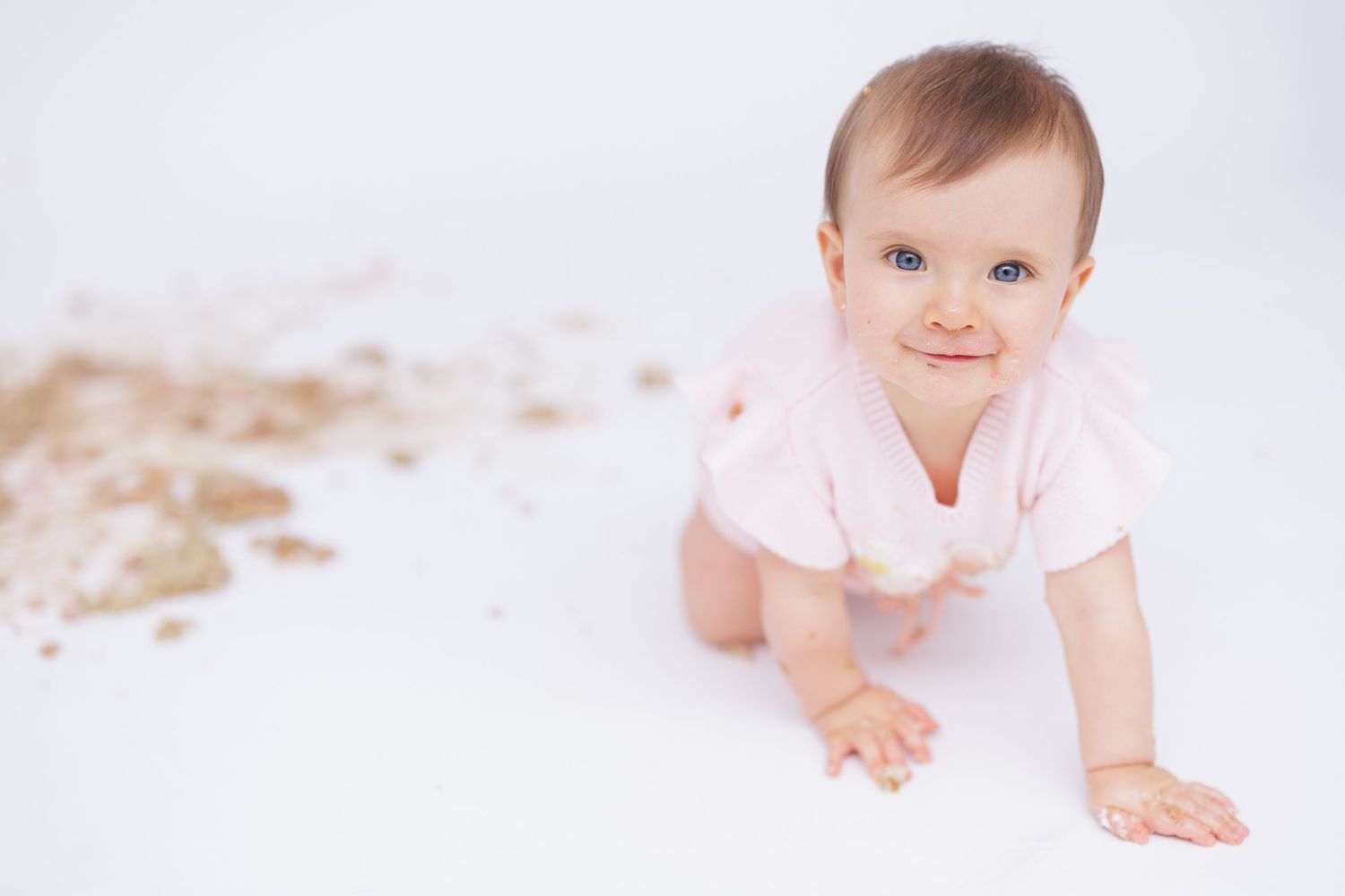 Baby in pink outfit crawling on white background during professional photo session.
