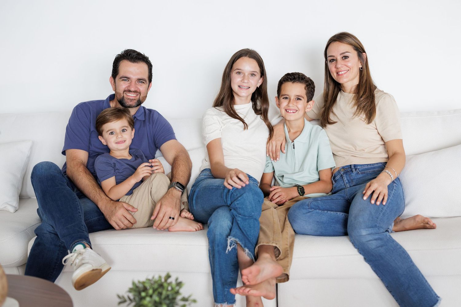 Family lounging together on white bedding in casual denim and neutral tones for a relaxed lifestyle photoshoot.