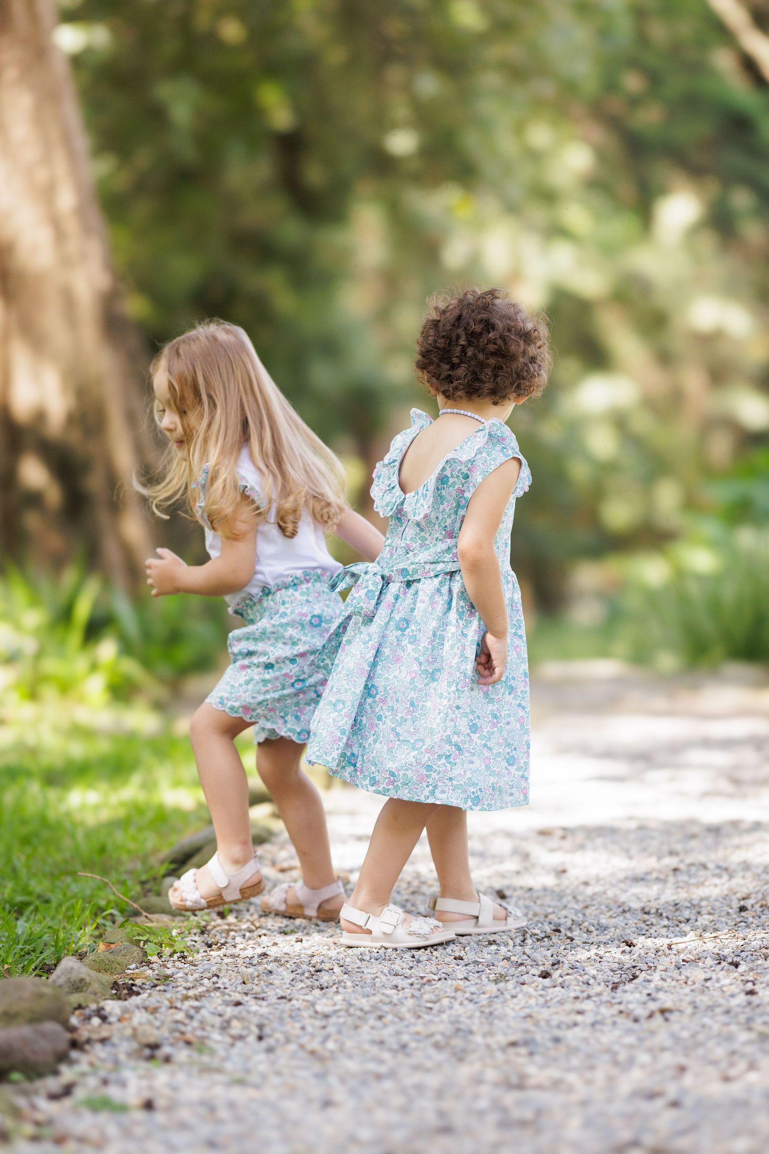 Children in matching blue dresses walk and play on gravel path outdoors.