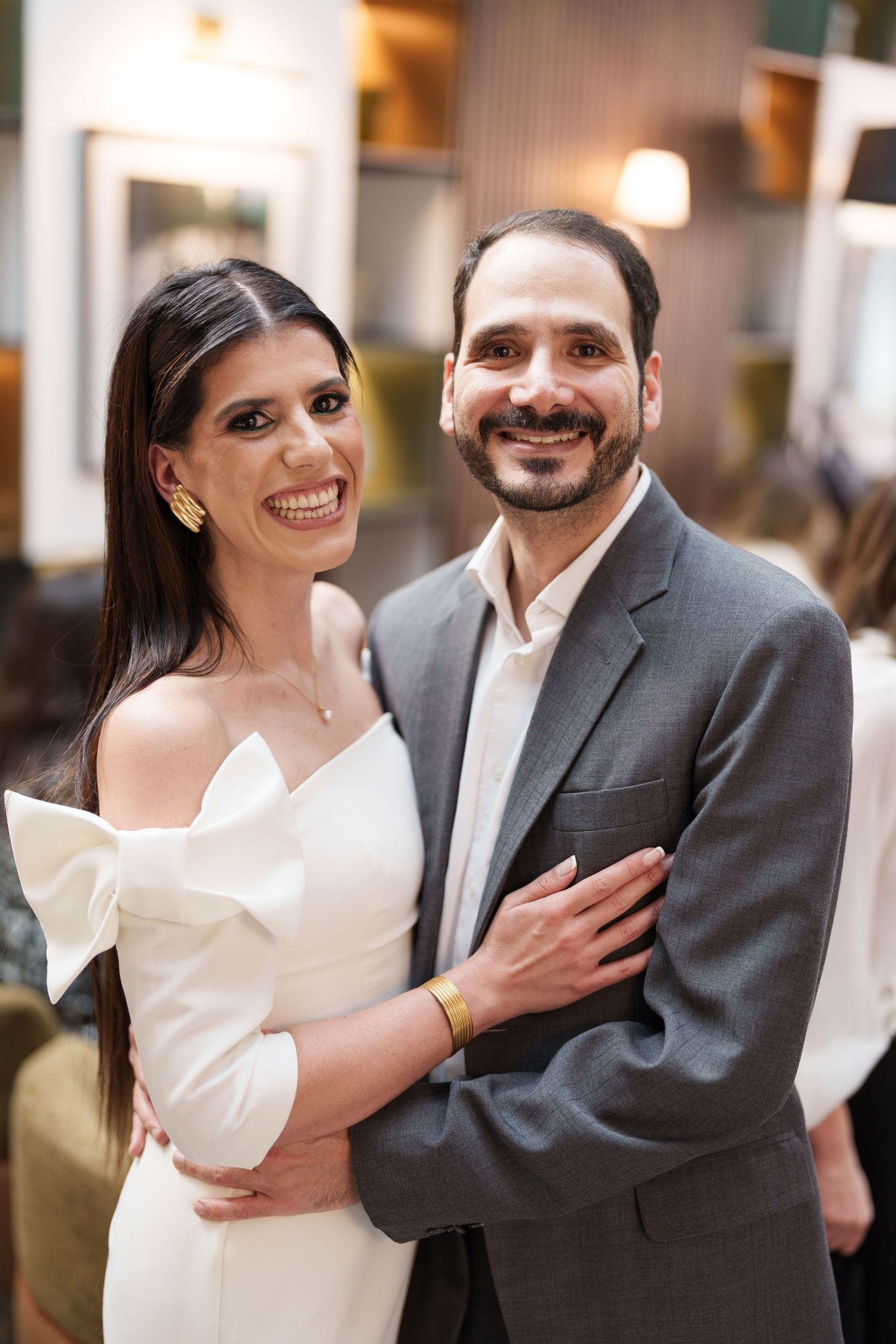 A couple in formal attire smiling together in an elegant indoor setting.