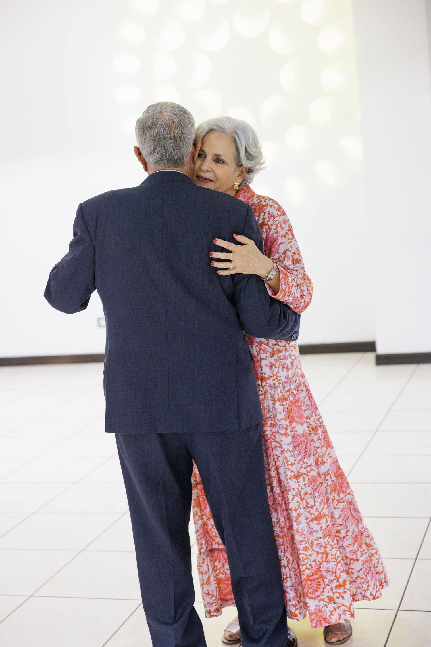 A couple in formal wear dancing together on a white tiled floor.