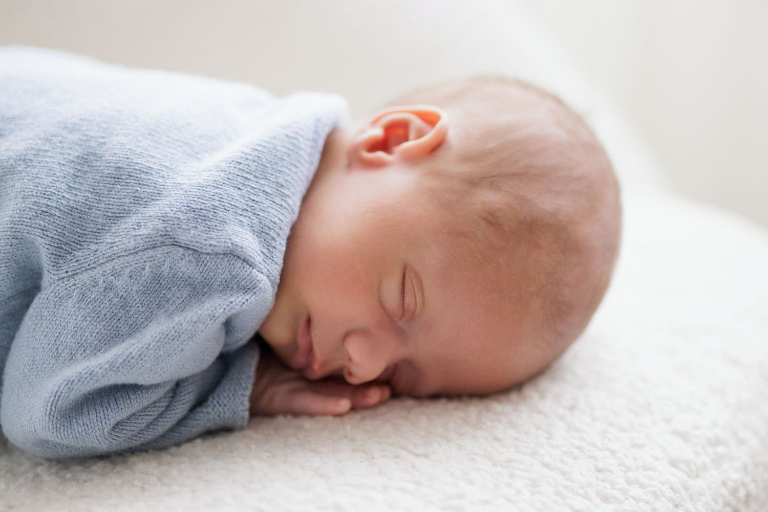 Sleeping newborn baby wearing gray outfit on textured white blanket.