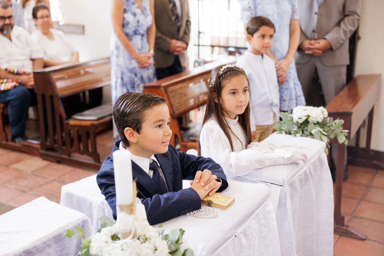 Children in formal white attire seated at an elegant reception table with floral decorations.