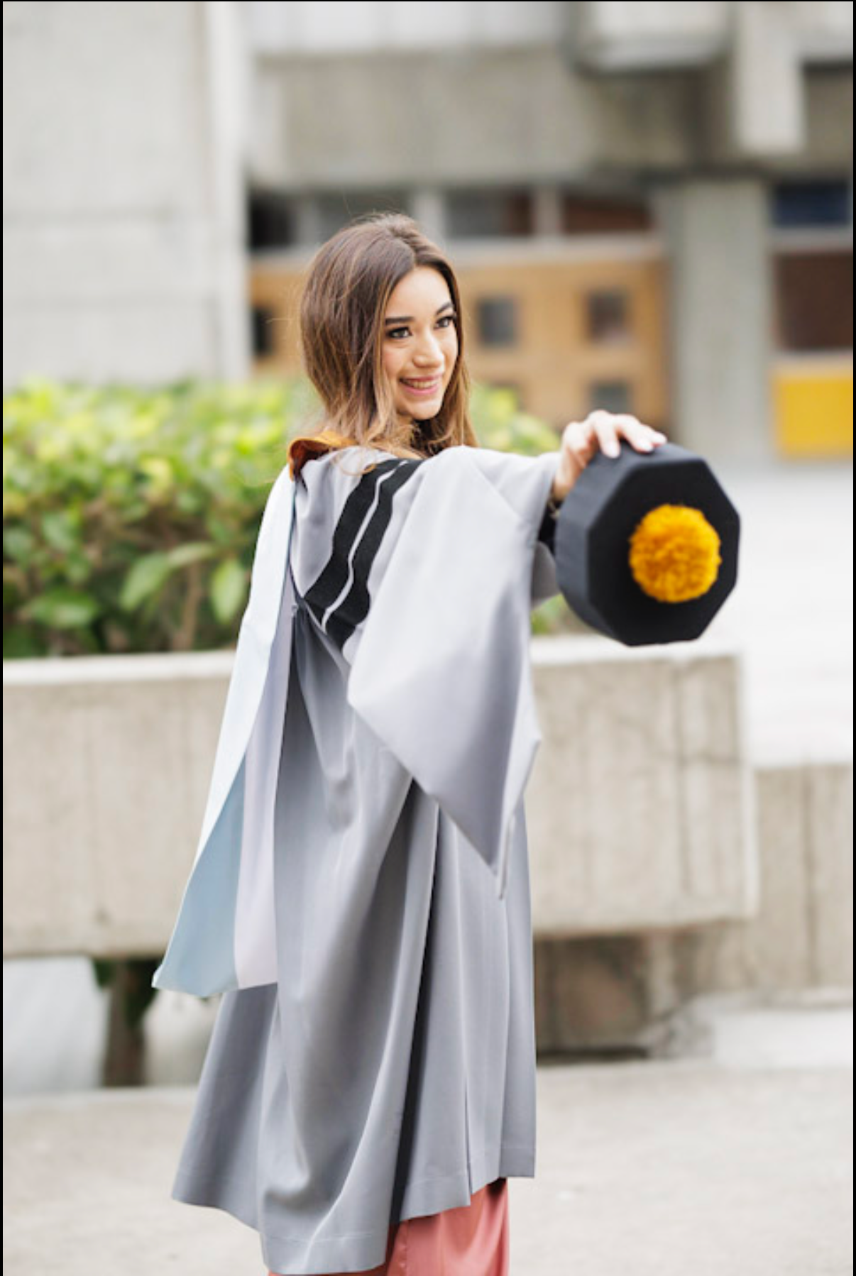 Graduate showcasing grey academic gown in outdoor portrait session.