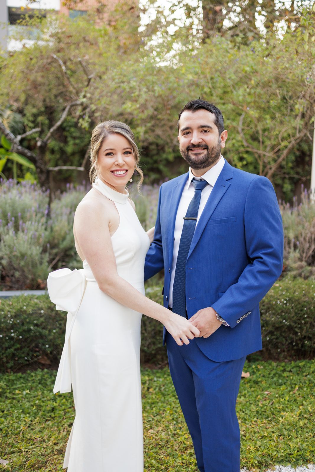 Wedding couple in classic white gown and royal blue suit pose together in a garden.