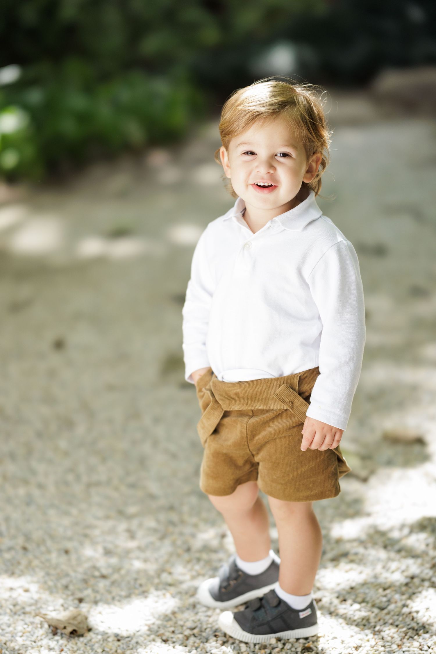 Child wearing white sweater and brown shorts walking on textured ground in natural lighting.