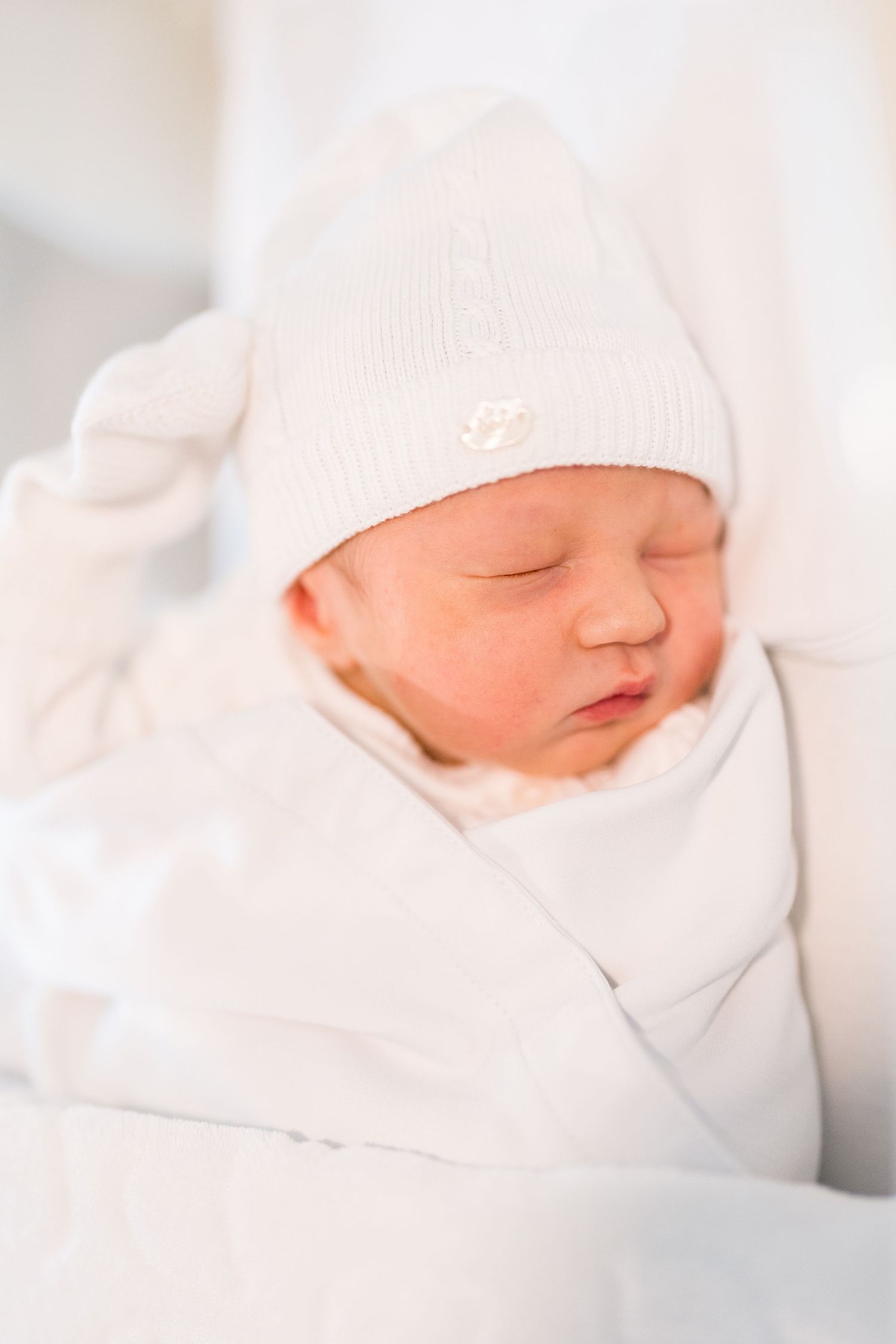 Sleeping newborn in white knit hat and clothing against white background.