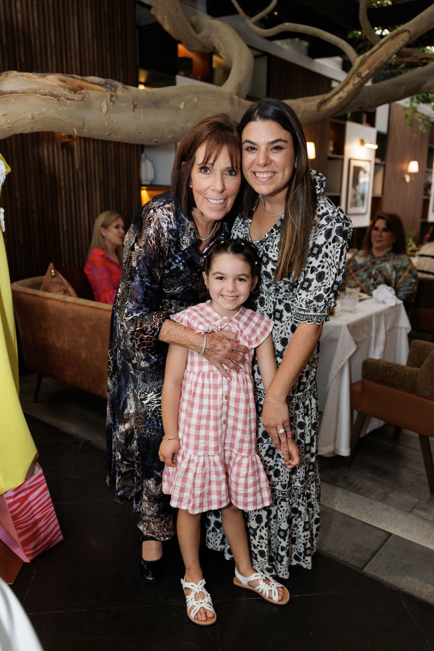 Three people pose together at a restaurant under decorative tree branches.