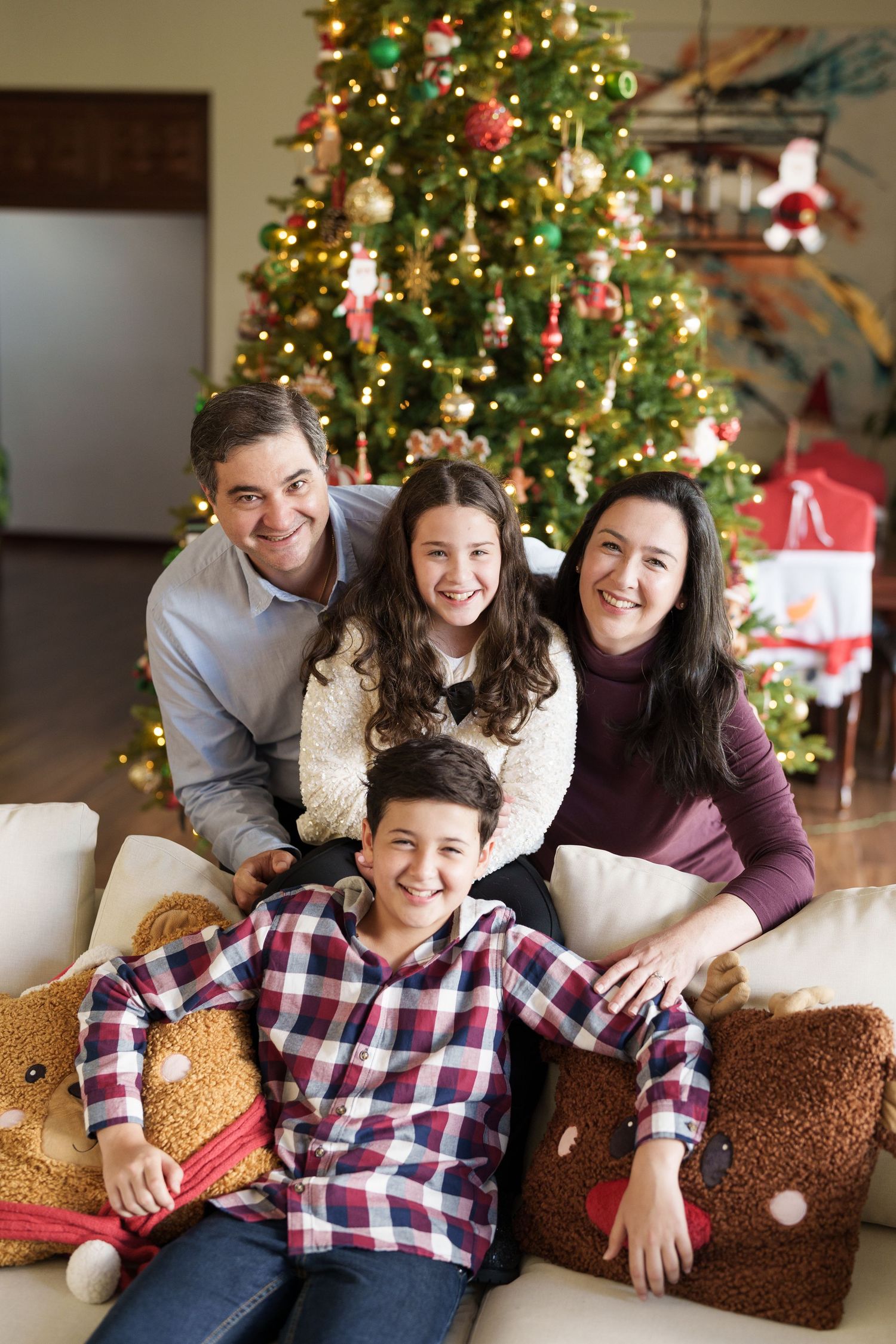 Holiday family portrait in front of Christmas tree with plaid shirts and cozy decor.