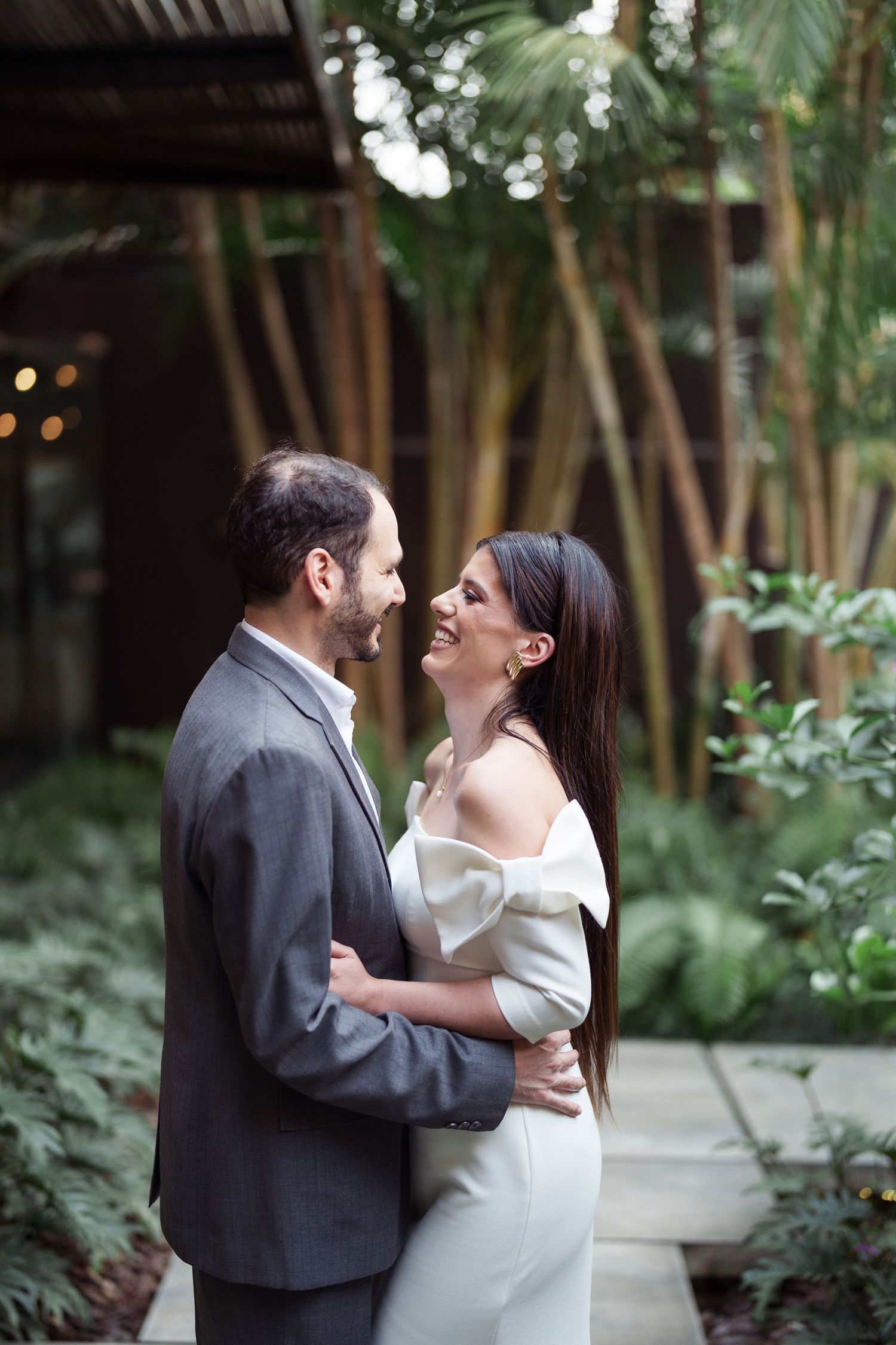 A romantic moment between a couple in formal wear surrounded by tropical greenery.