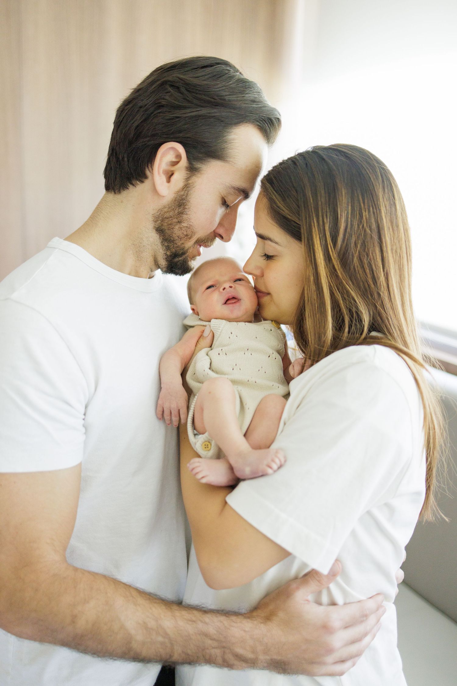 Family sharing intimate moments in white clothing against light background.