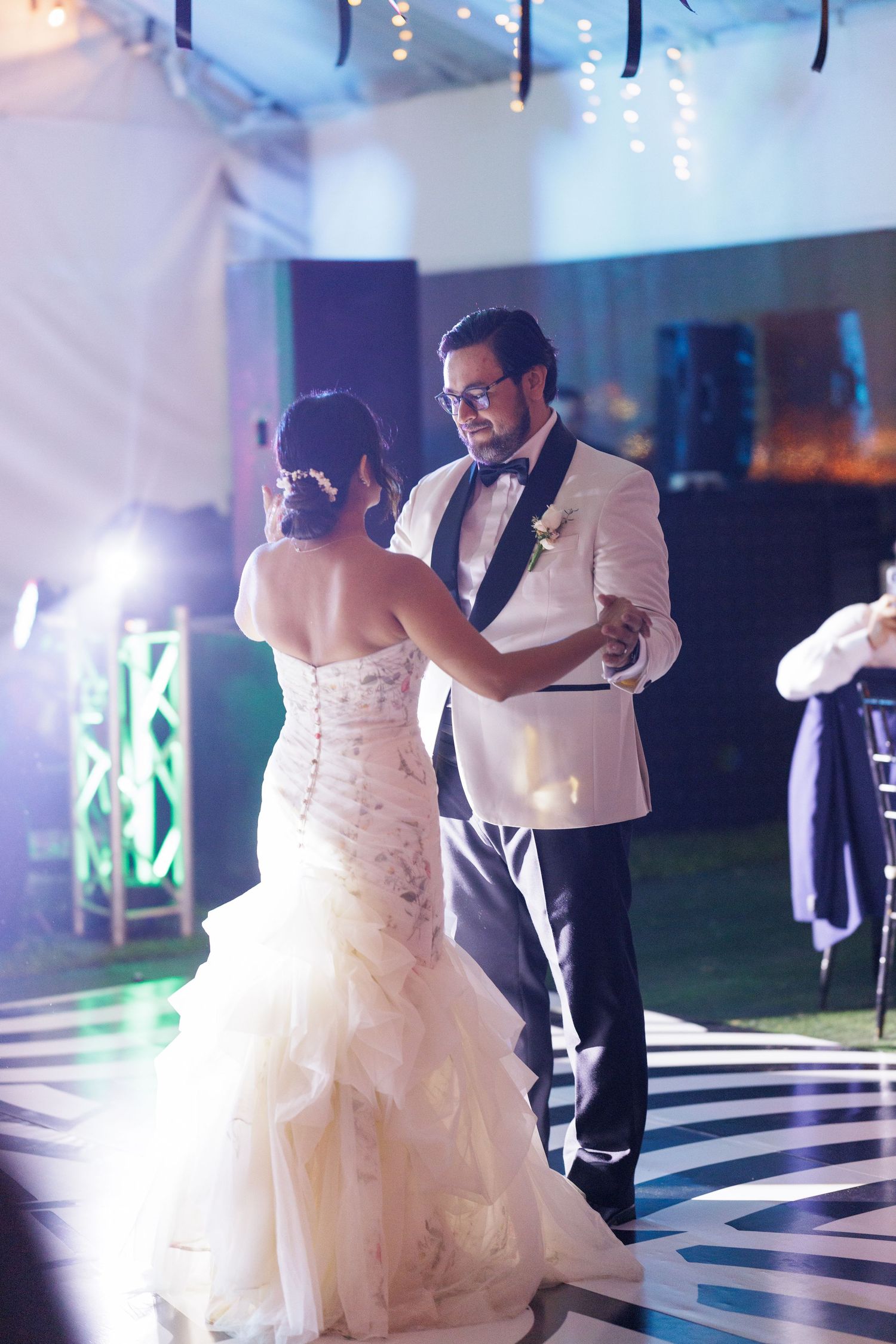 Couple dancing on a black and white checkered dance floor under blue lighting at their reception.