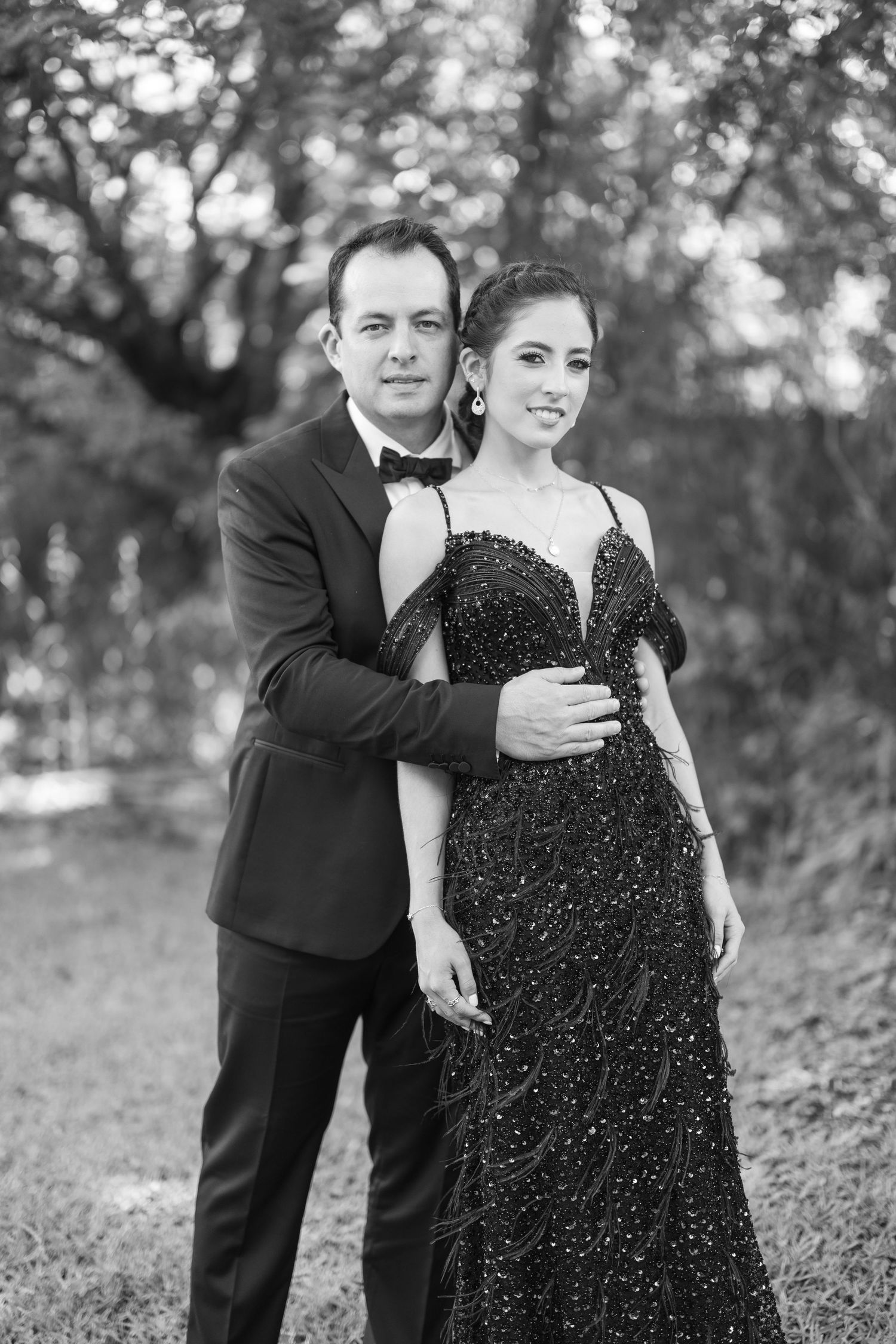 A couple in formal attire embraces during an outdoor black and white photo session.