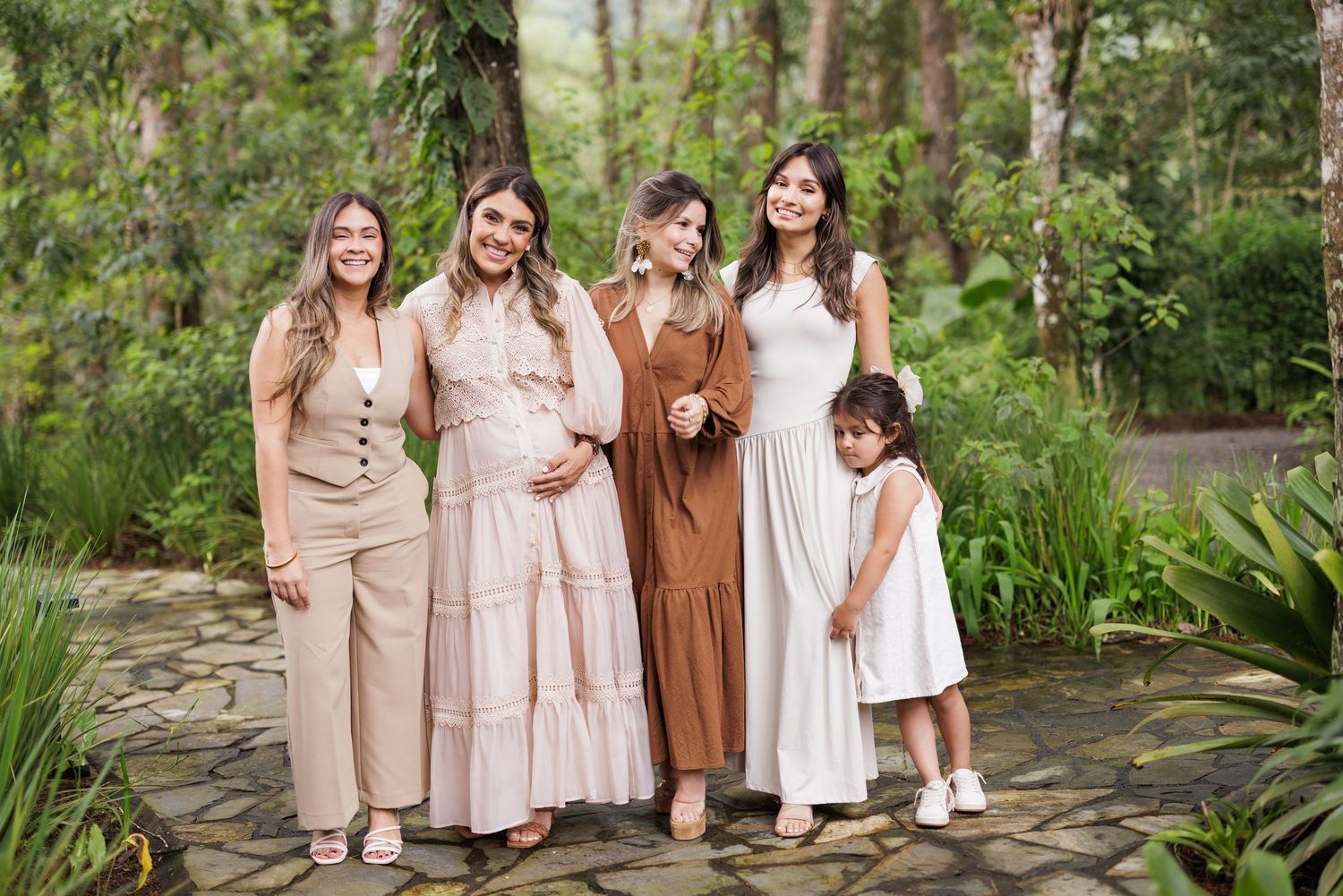 A group poses outdoors wearing coordinated neutral toned dresses in a garden setting.