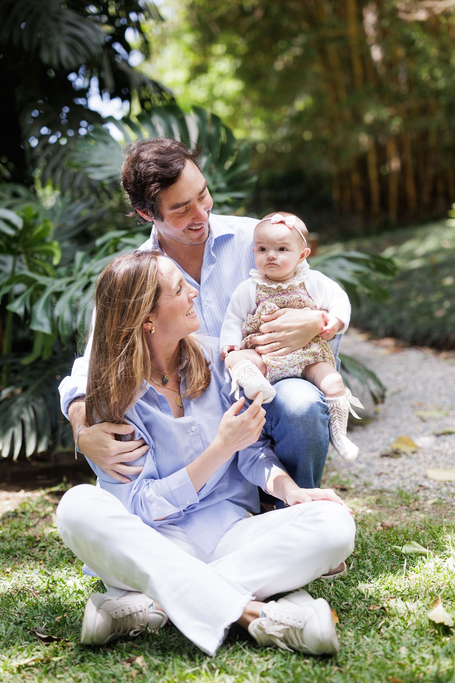 Family relaxing together on grass in white outfits during outdoor photoshoot.