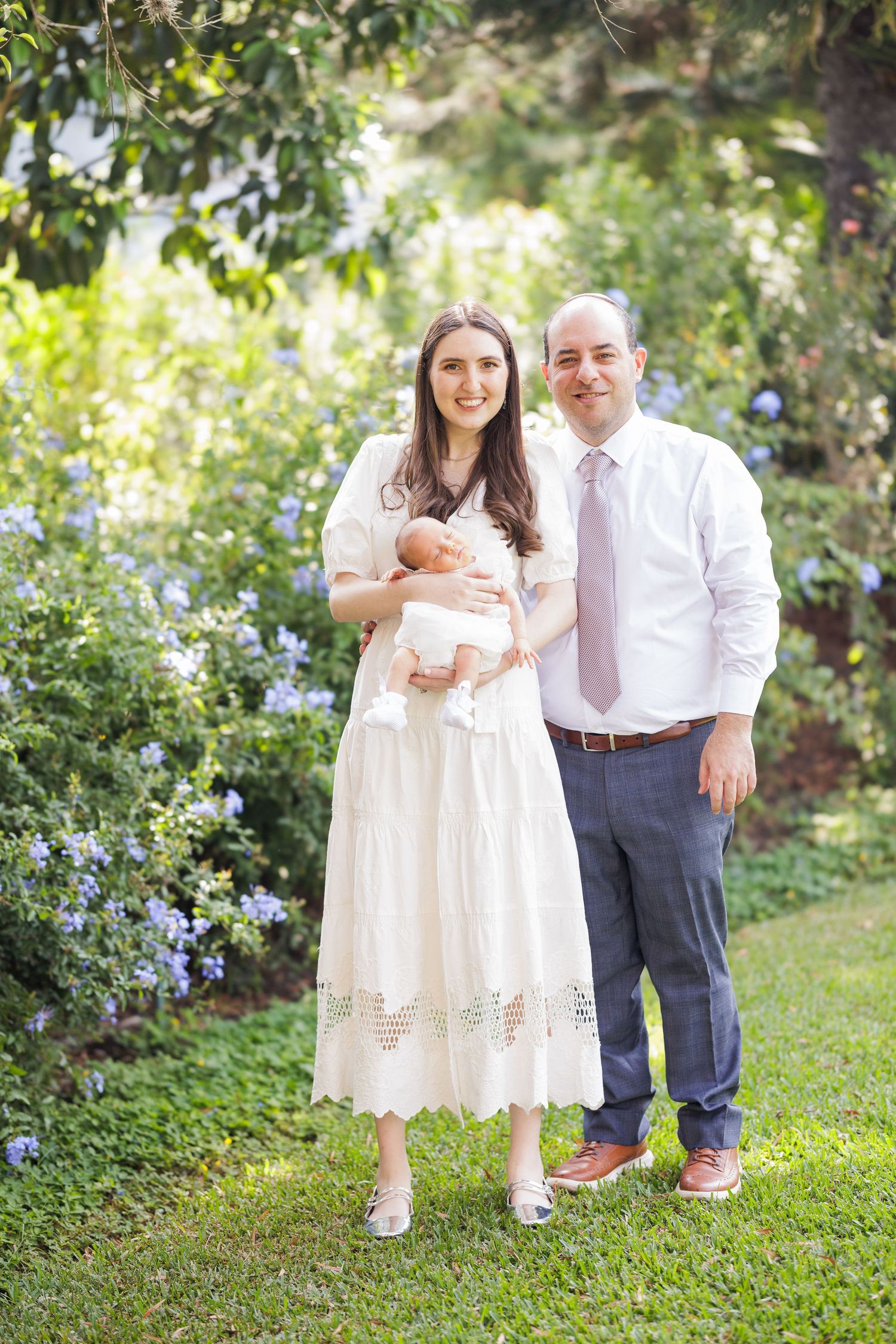 A couple in white and navy attire pose together in a garden setting.