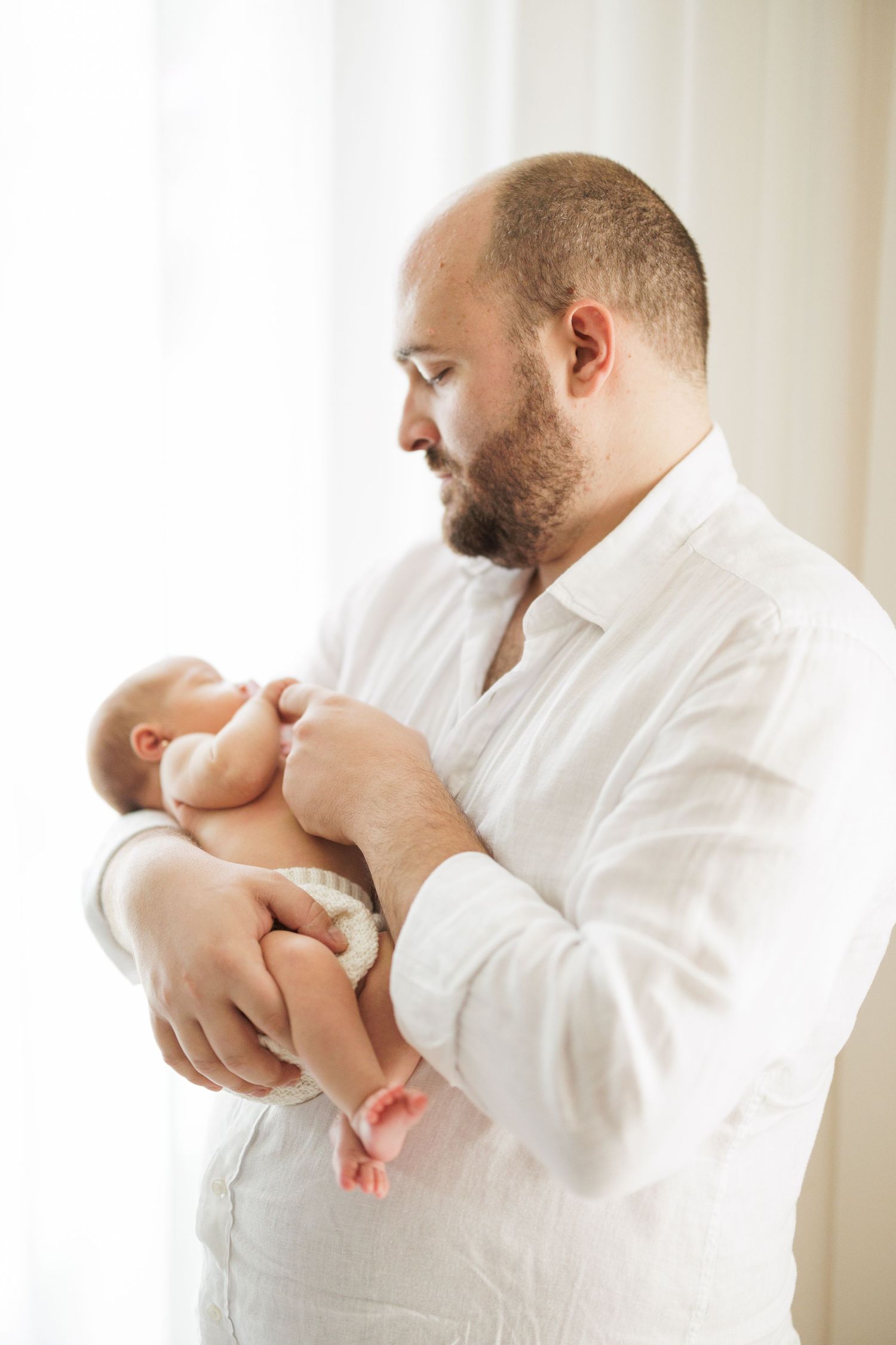 Parent in white shirt tenderly holding and bonding with newborn baby against bright background.