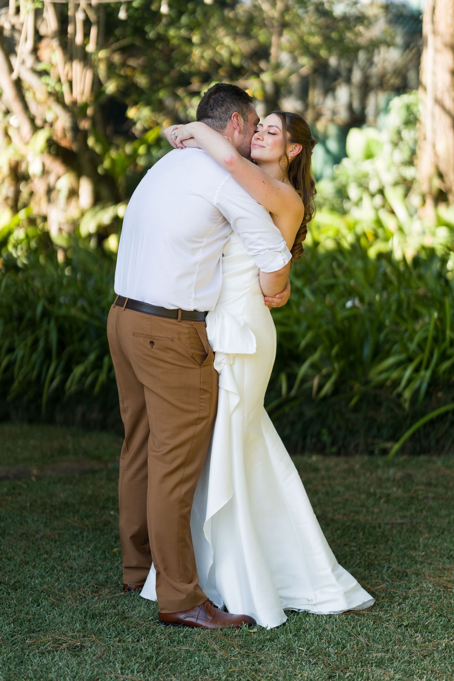 Wedding couple dancing together on grass in casual wedding attire.