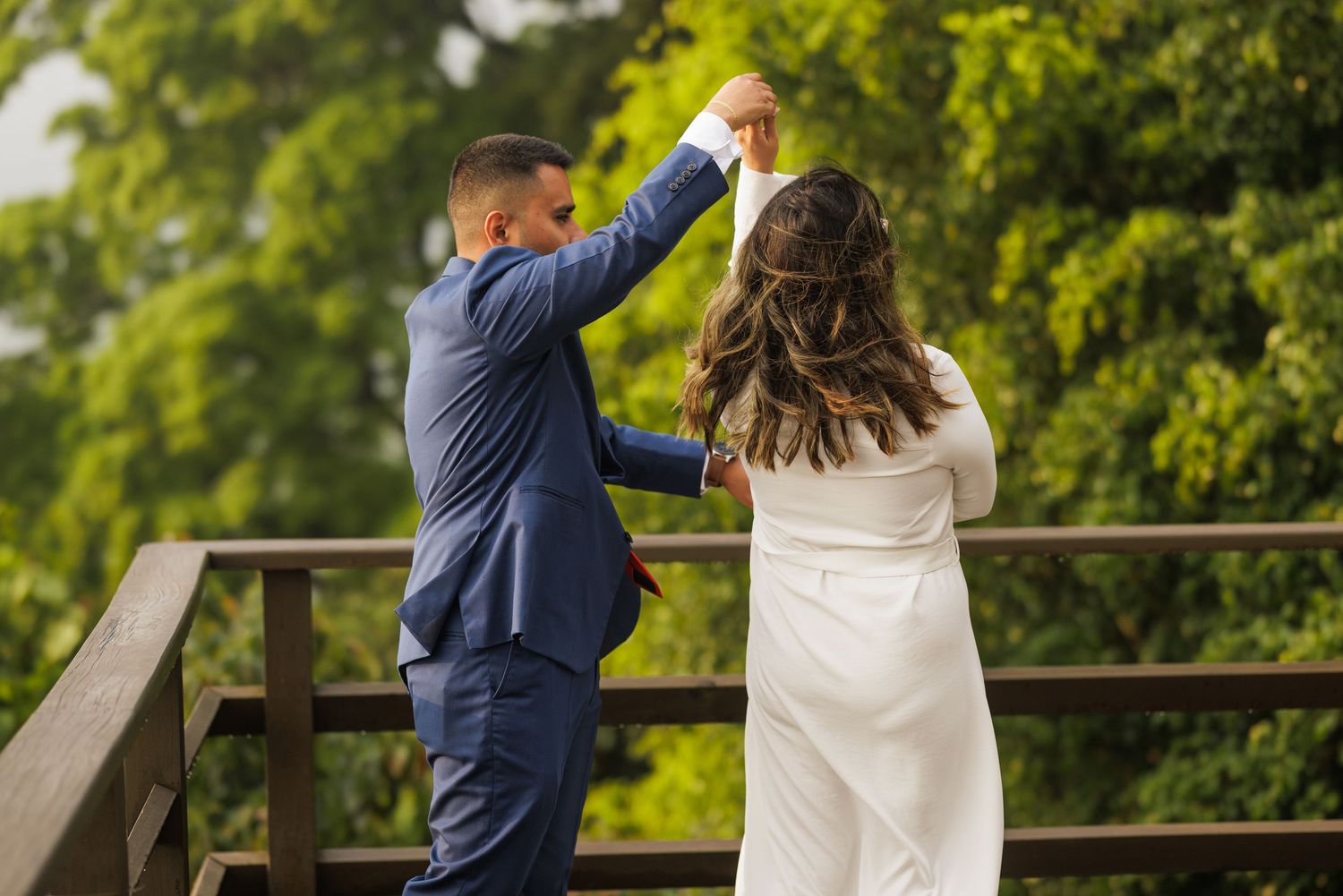 A couple dancing together on a wooden deck surrounded by lush green trees.