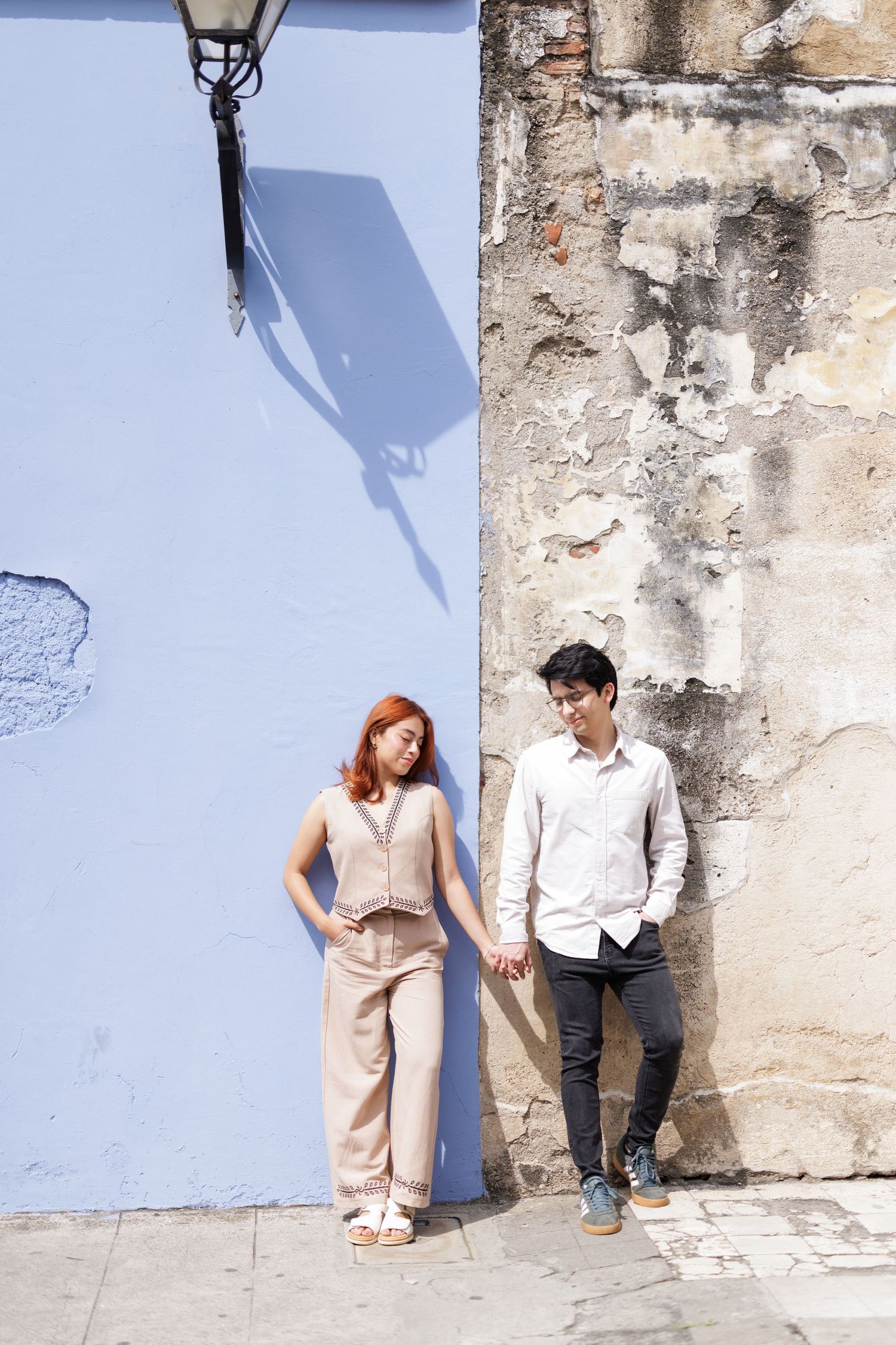 Romantic couple poses against weathered wall with dramatic shadows.