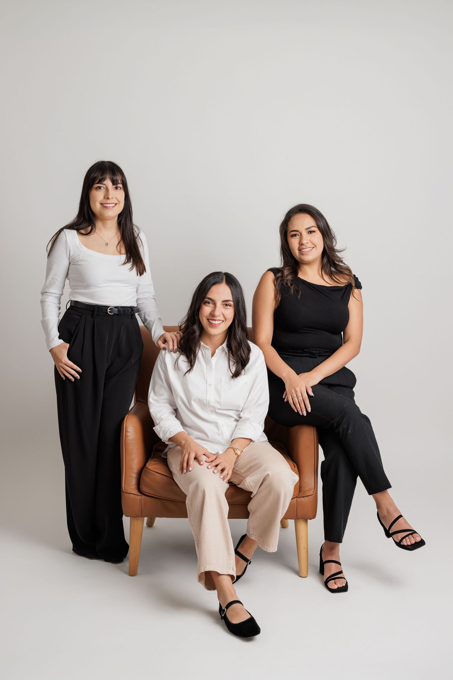 Group photo of people in business casual attire sitting on brown leather chair against white backdrop.