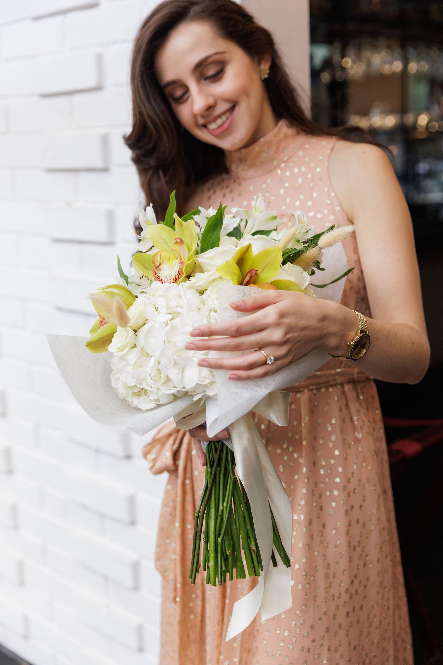 Person in blush dress holding a white and yellow lily bouquet.