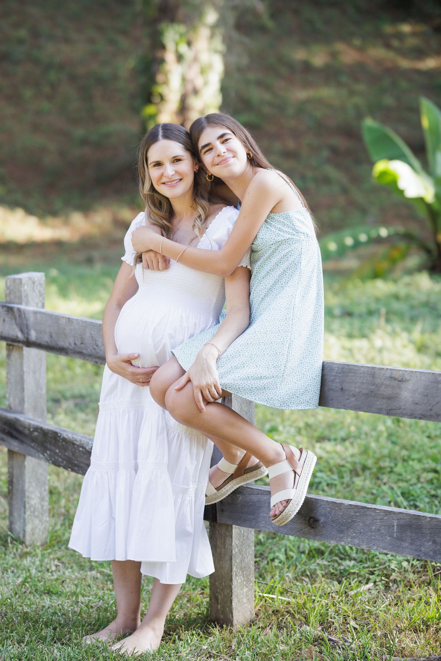 Two people share tender moments while sitting on a wooden fence in a pastoral setting.