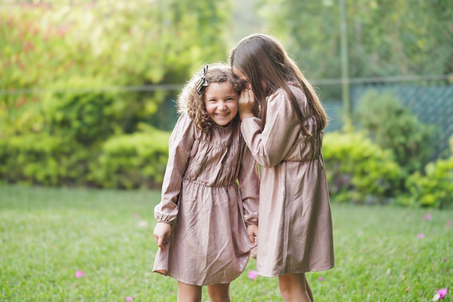 Two young children walk together through lush garden setting.