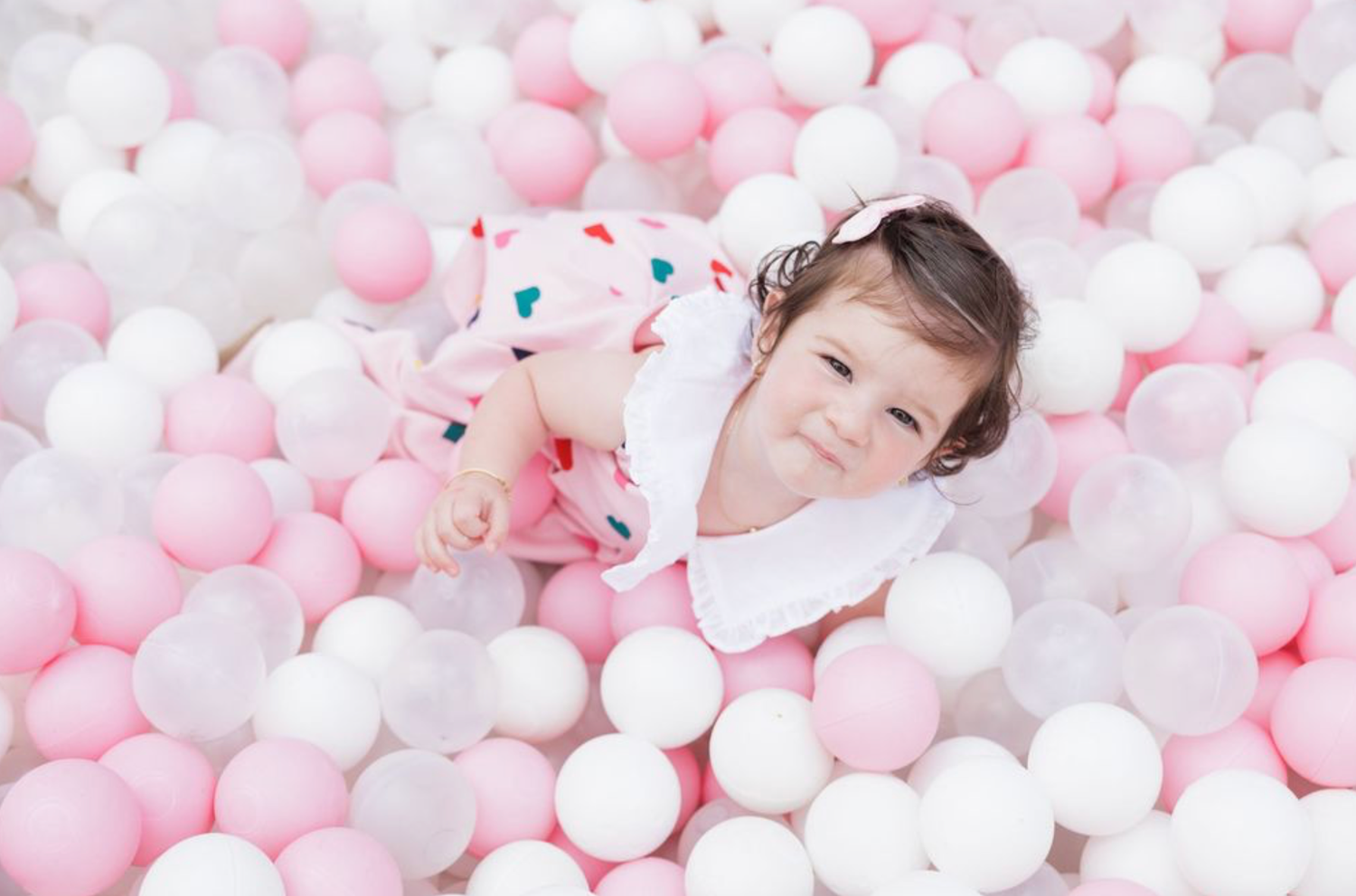 A person relaxes in a ball pit filled with pink and white balls.
