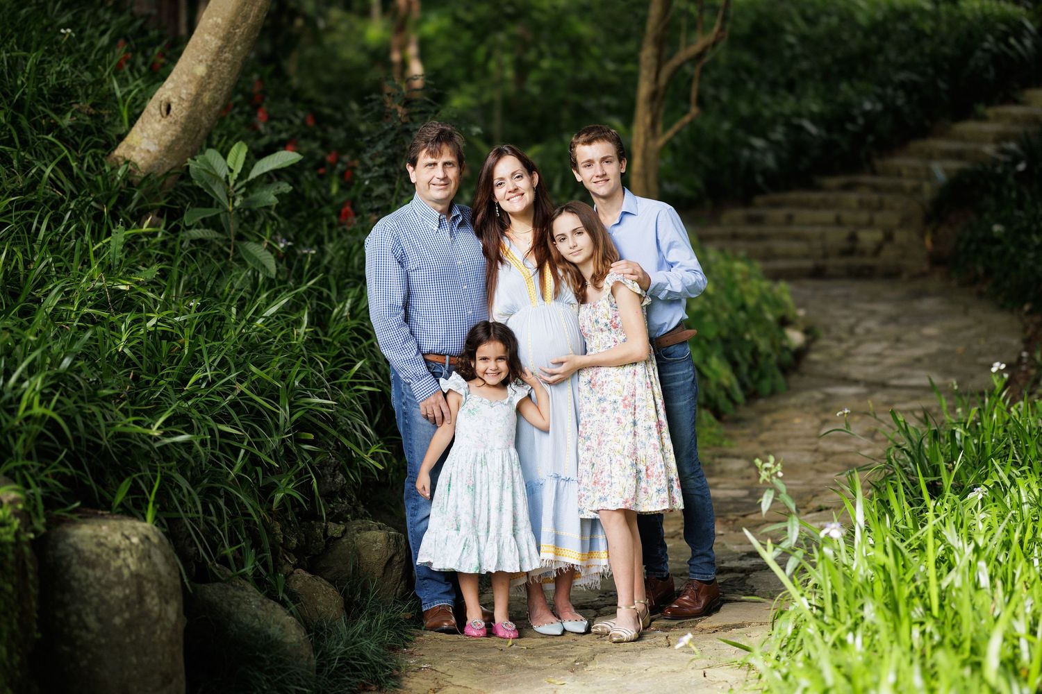 Family portrait session in a garden setting with stone steps and lush greenery.