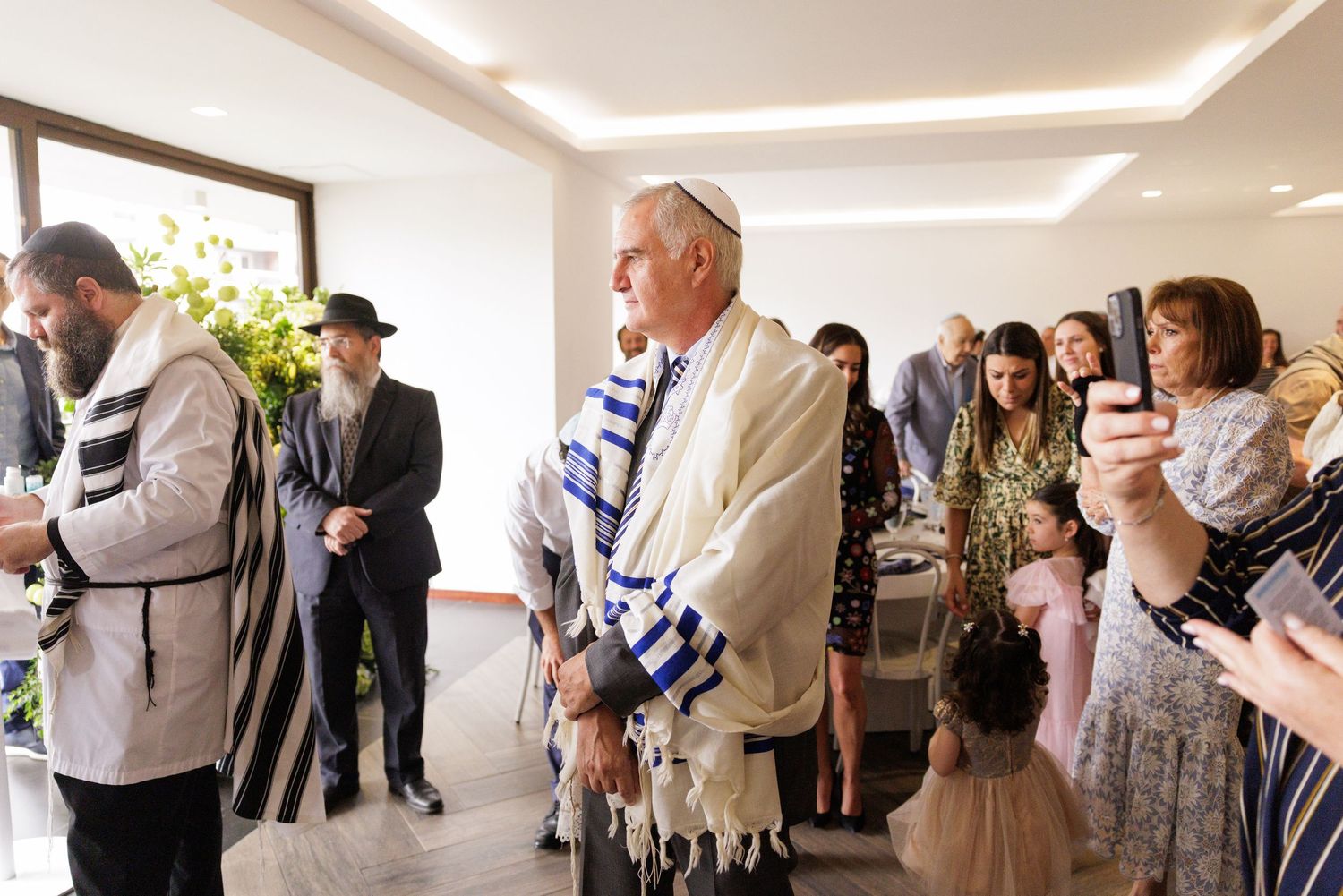 Guests in traditional religious attire gather at a modern celebration venue with natural lighting.