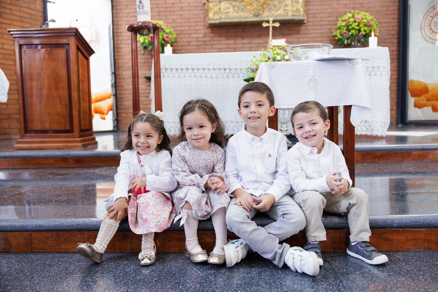 Children in white outfits sit together on church steps during a special occasion.