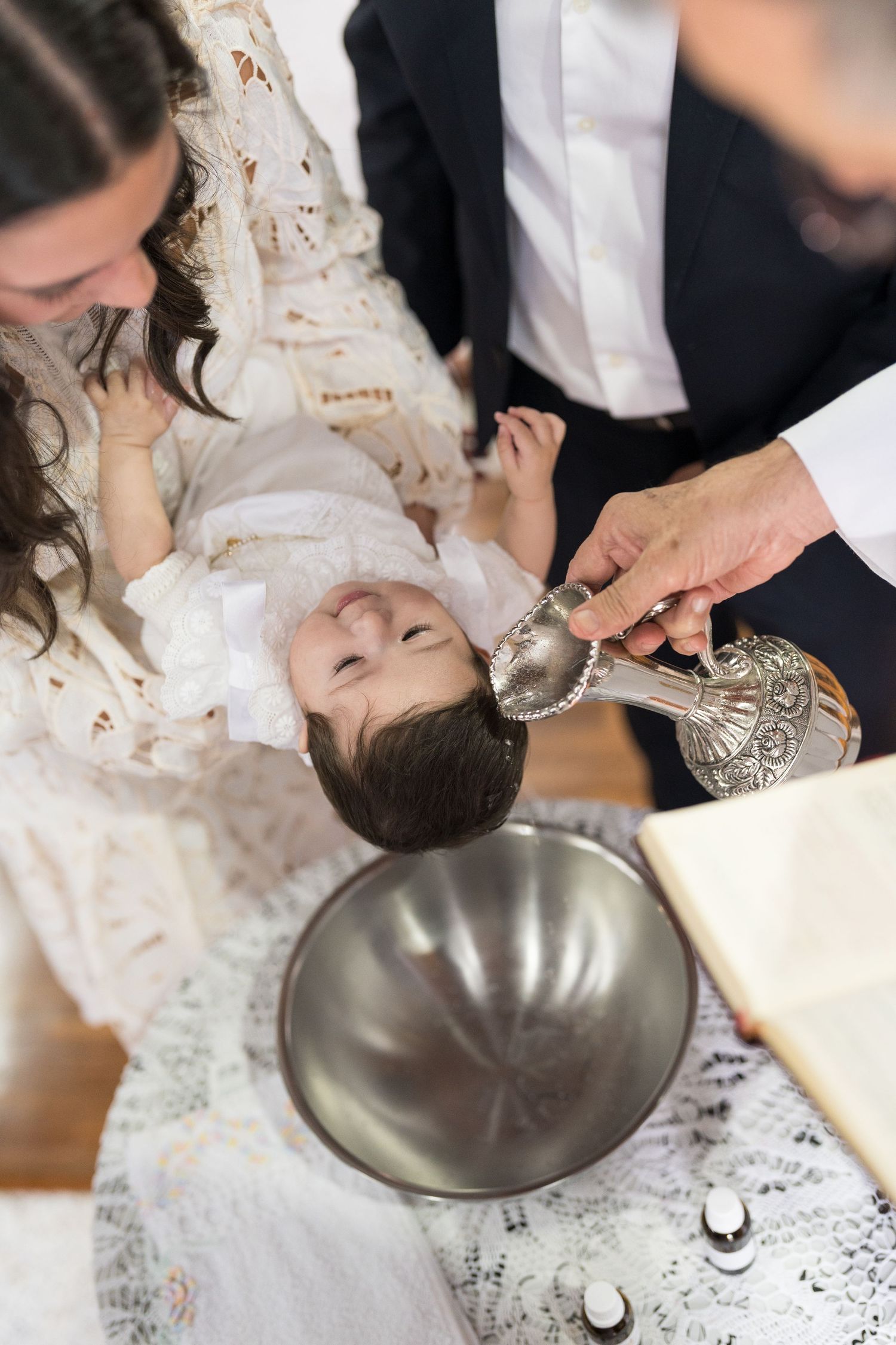 Close-up of a traditional baptism ceremony with silver ceremonial items on white lace.
