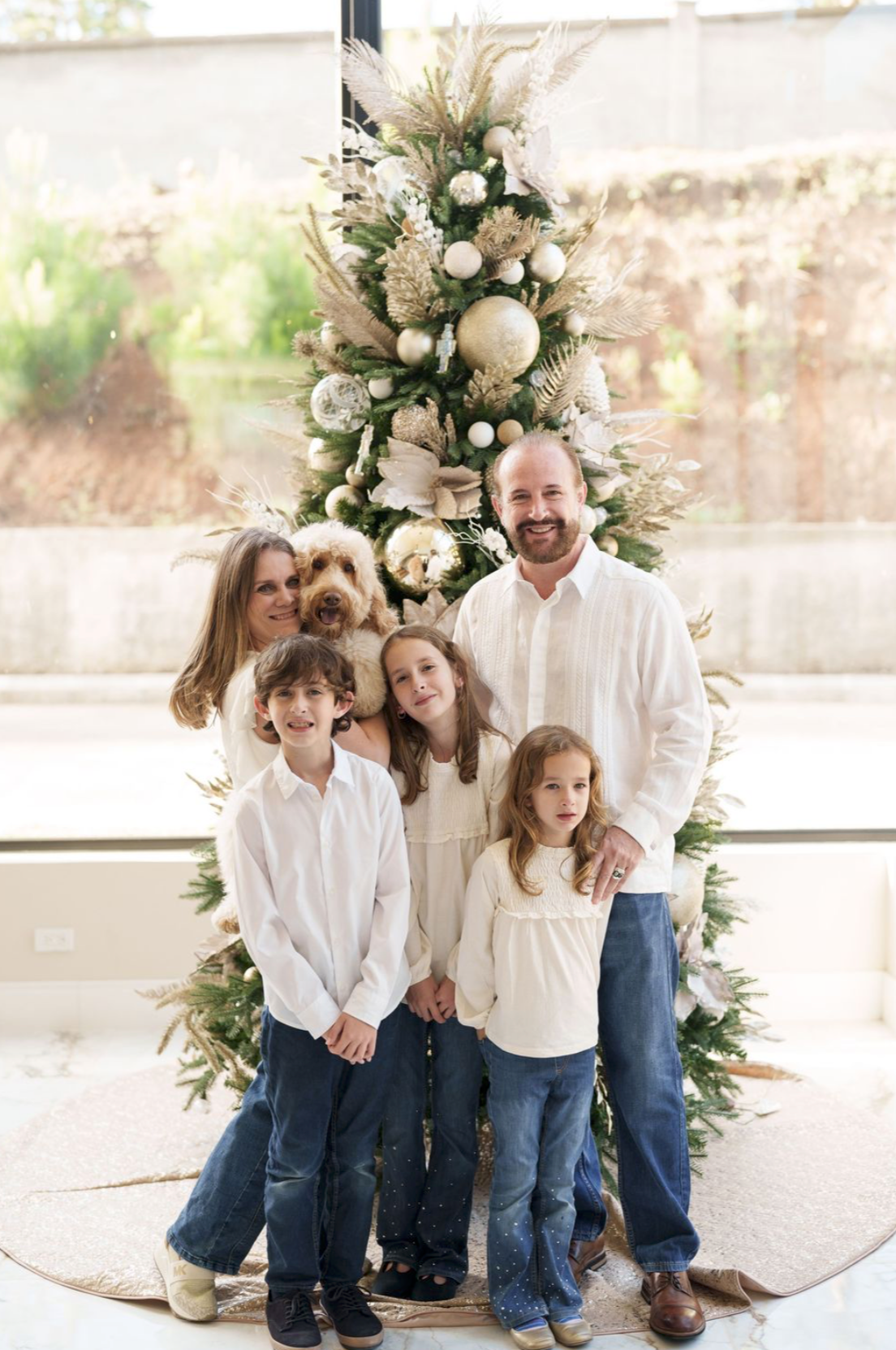 Family in coordinated white and denim outfits poses together against floral backdrop.