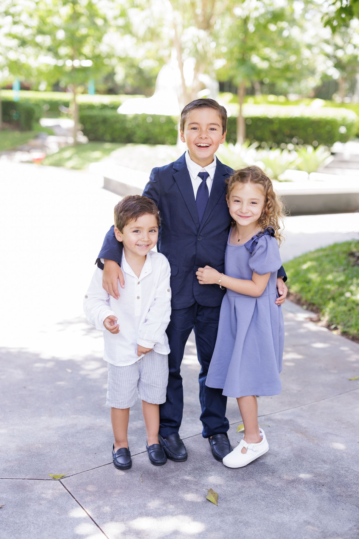 Children in formal attire stand together on a concrete path.
