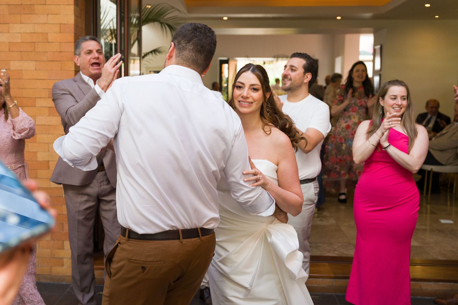 Wedding guests dancing and celebrating at a reception with brick walls and festive lighting.