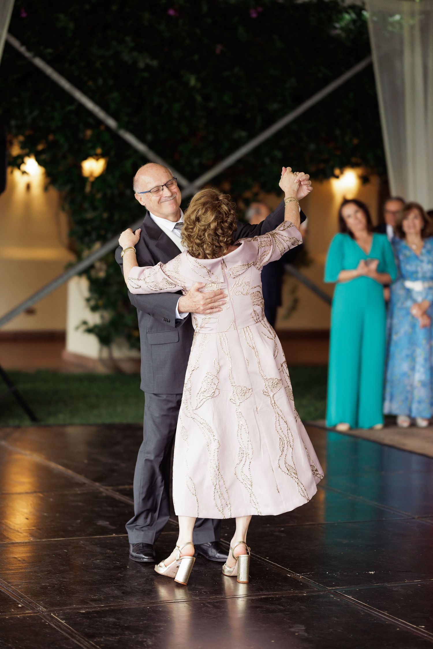 People dancing on a dark wooden dance floor at an evening celebration.