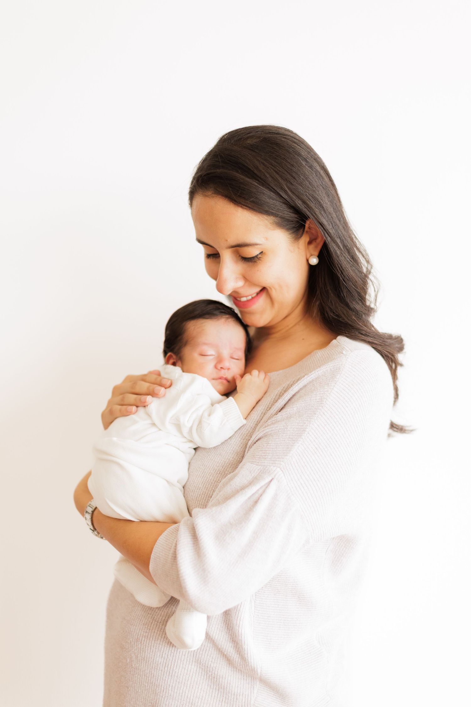 Mother in white shirt tenderly holding and gazing at newborn baby against neutral background.