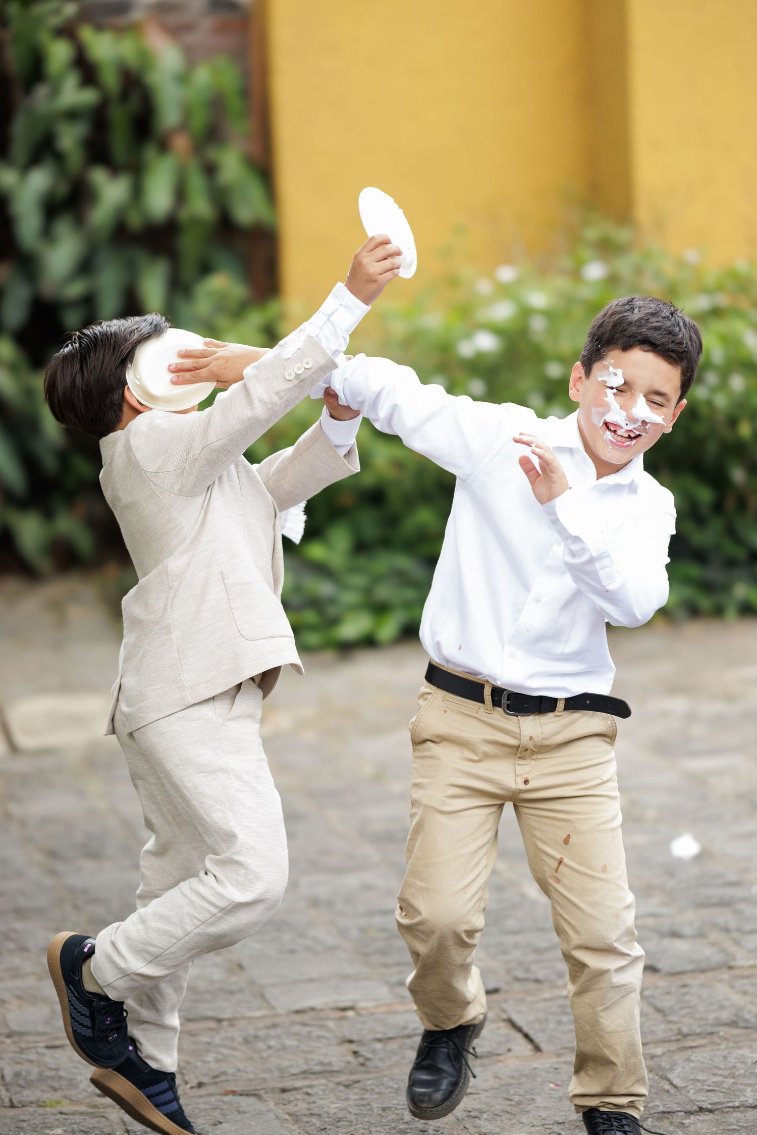Two children in white and khaki outfits dance and play on a stone patio.