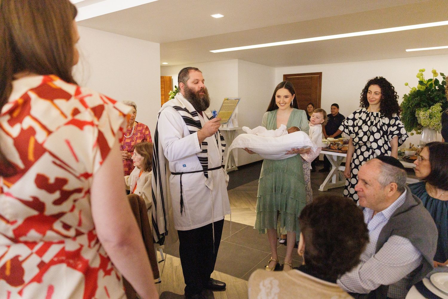 A religious ceremony takes place in a bright modern venue with guests seated at tables.