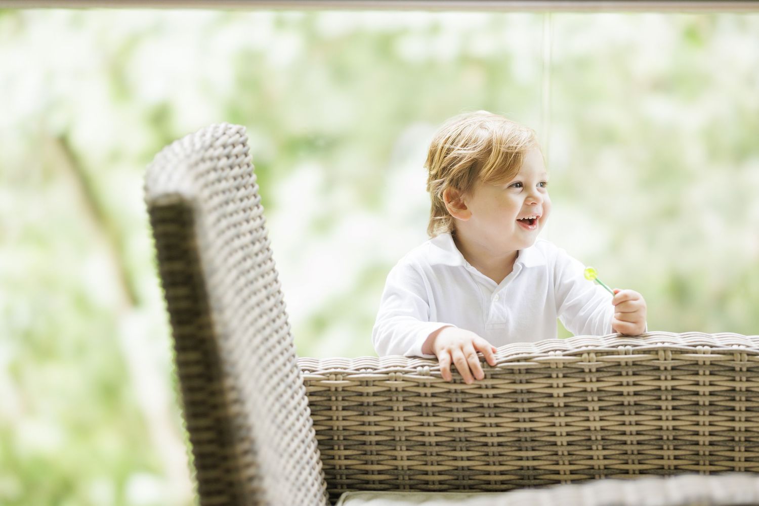 Child laughing while sitting in wicker chair outdoors in natural setting.