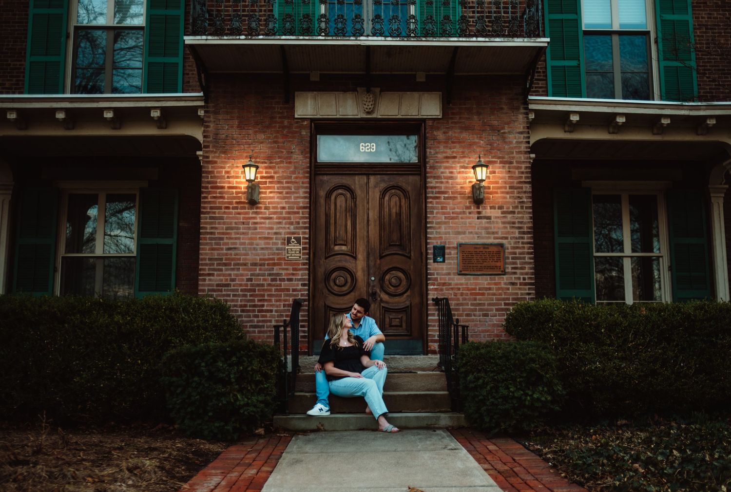 Couple sharing a romantic embrace on brick steps of a charming historic building at dusk with warm lantern lighting.