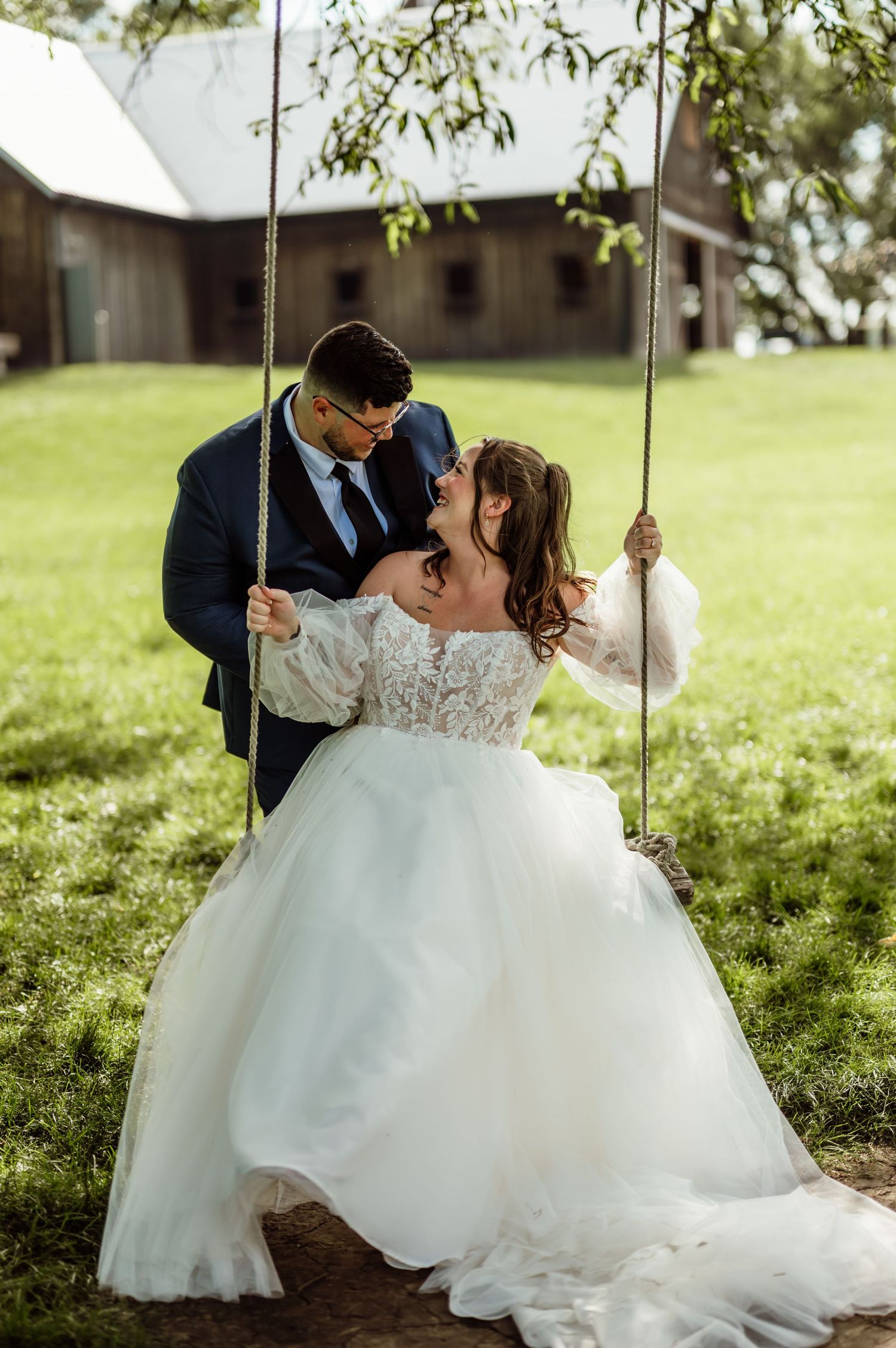 Bride sits on rope swing as groom leans in for a kiss at Kennedy Estate in Lizton, Indiana